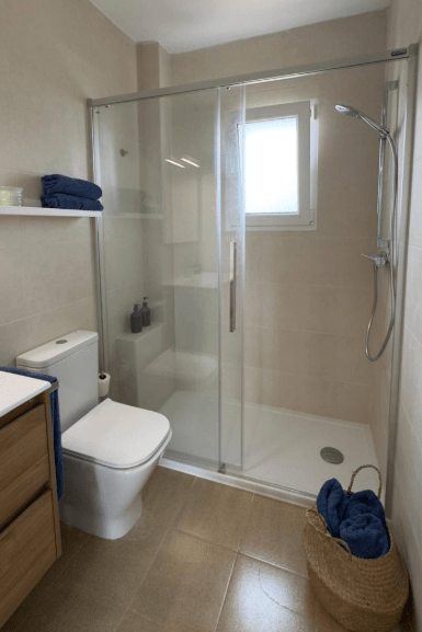 Modern bathroom featuring a glass shower enclosure, toilet, and wooden storage unit, with navy blue towels displayed.