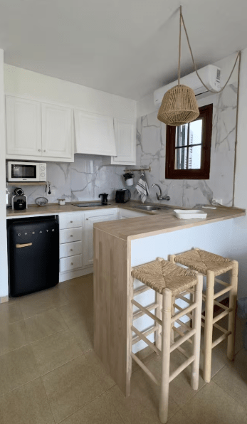 Modern kitchen with white cabinets, marble-patterned walls, black refrigerator, and wooden bar with two stools.