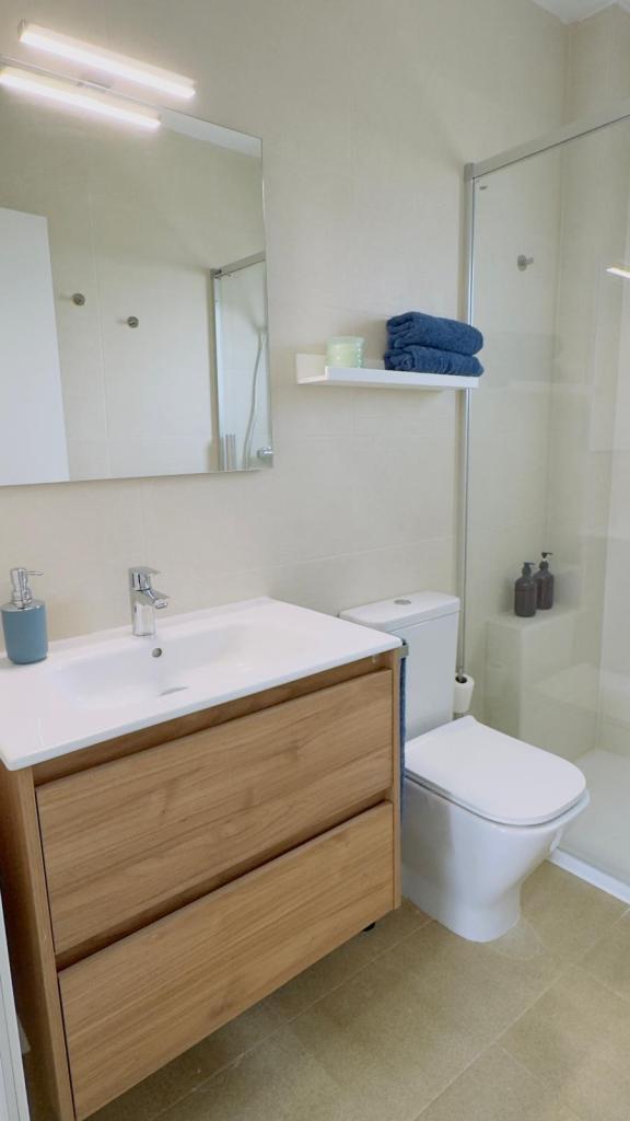 Modern bathroom featuring a wooden vanity with a sink, a toilet, and a shower enclosure. Towels are neatly arranged on a shelf.